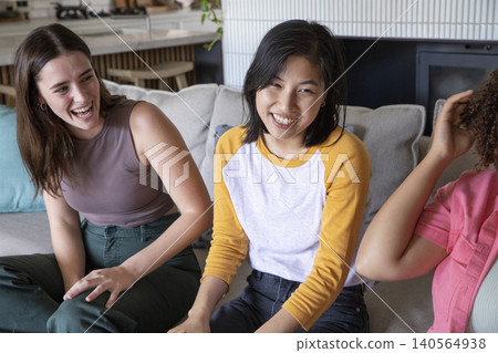 Diverse female friends sitting on light sofa in lounge with cushions, bar stools and hanging plant Diverse female friends sitting on light sofa in lounge with cushions, bar stools and hanging plant 140564938
