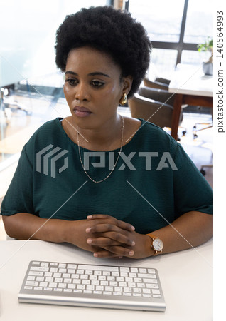 African american woman sitting at office desk in green blouse typing with wireless keyboard African american woman sitting at office desk in green blouse typing with wireless keyboard 140564993
