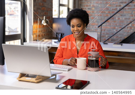 African american woman holding mug and french press, typing on keyboard in loft office African american woman holding mug and french press, typing on keyboard in loft office 140564995