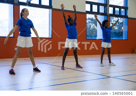 Diverse female students warming up in school gym on wooden court with lines and windows Diverse female students warming up in school gym on wooden court with lines and windows 140565001
