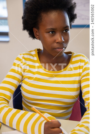 African american teen student writing with pencil on paper in classroom with whiteboard African american teen student writing with pencil on paper in classroom with whiteboard 140565002