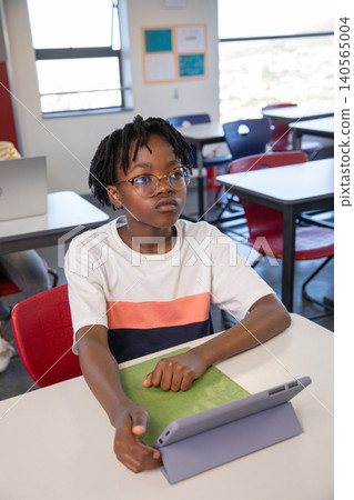 African american child sitting in red chair at desk in classroom using tablet in case African american child sitting in red chair at desk in classroom using tablet in case 140565004