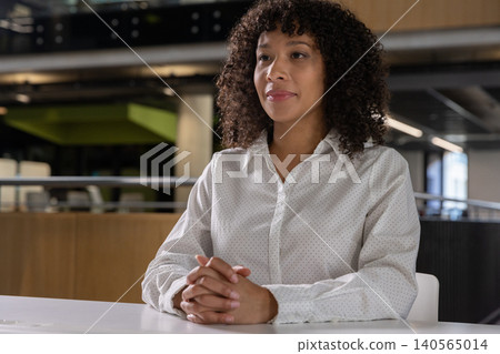 African american woman sitting at white table in office in white blouse with metal railing African american woman sitting at white table in office in white blouse with metal railing 140565014