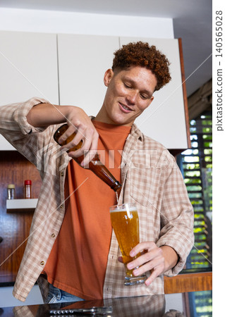 Red-haired man pouring beer from bottle into pilsner glass in kitchen with metal opener Red-haired man pouring beer from bottle into pilsner glass in kitchen with metal opener 140565028