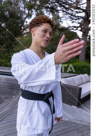 Male martial artist initiating sparring stance wearing gi and belt on deck by pool Male martial artist initiating sparring stance wearing gi and belt on deck by pool 140565032