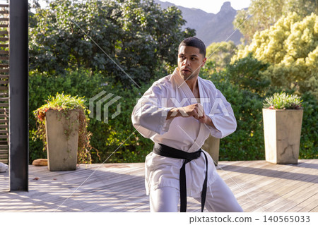 African american man training martial arts in white gi, black belt on deck with planters African american man training martial arts in white gi, black belt on deck with planters 140565033