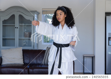 African american woman practicing punch stance in living room wearing karate gi and belt African american woman practicing punch stance in living room wearing karate gi and belt 140565035