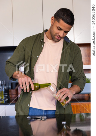 Man pouring beer from green bottle into tall glass on dark countertop at kitchen island Man pouring beer from green bottle into tall glass on dark countertop at kitchen island 140565040