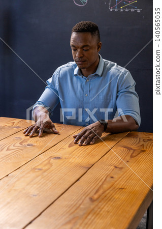 African american man sitting at wooden table reviewing chalkboard graphs African american man sitting at wooden table reviewing chalkboard graphs 140565055