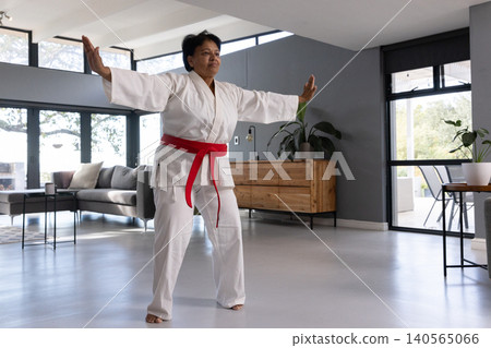 Senior asian indian woman performing martial arts kick in living room with gi and belt Senior asian indian woman performing martial arts kick in living room with gi and belt 140565066