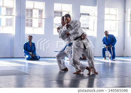 Male martial arts students grappling on tatami mats at dojo in white gis and colored belts Male martial arts students grappling on tatami mats at dojo in white gis and colored belts 140565096