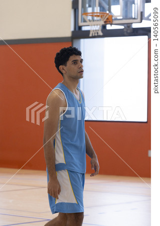 Male basketball player standing in gym court on polished court looking toward hoop Male basketball player standing in gym court on polished court looking toward hoop 140565099