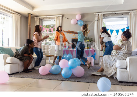 Diverse female friends with infants gathering next to pastel party table and balloons Diverse female friends with infants gathering next to pastel party table and balloons 140565174