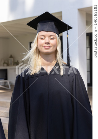 Female graduate standing in front of university porch wearing mortarboard cap, black gown Female graduate standing in front of university porch wearing mortarboard cap, black gown 140565183