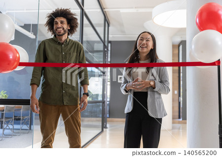 Diverse coworkers cutting red ribbon in modern office lobby with balloons Diverse coworkers cutting red ribbon in modern office lobby with balloons 140565200