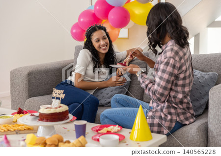 Diverse mom and teenage daughter sitting on couch for birthday sharing velvet cake slice Diverse mom and teenage daughter sitting on couch for birthday sharing velvet cake slice 140565228