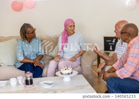 Diverse friends gathering around table at home with cake, coffee mugs, cancer survivor sign Diverse friends gathering around table at home with cake, coffee mugs, cancer survivor sign 140565233