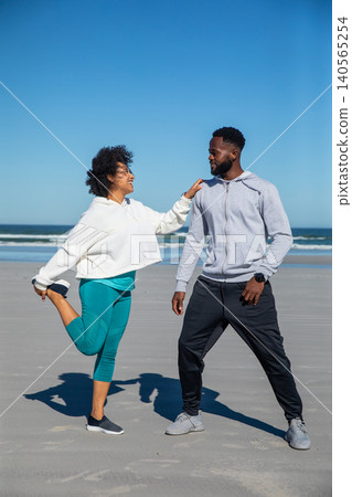 Diverse couple stretching quads on sandy beach wearing hoodies, leggings, sneakers, smartwatch Diverse couple stretching quads on sandy beach wearing hoodies, leggings, sneakers, smartwatch 140565254