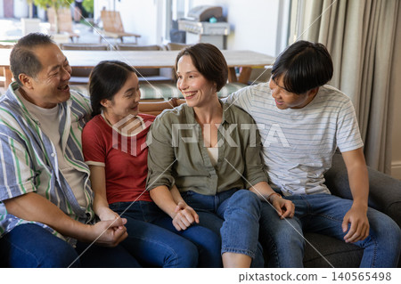 Diverse family sitting on gray couch in living room, smiling and interacting with cushions Diverse family sitting on gray couch in living room, smiling and interacting with cushions 140565498