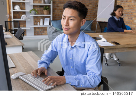 Asian coworkers typing on keyboard at open-plan office desk, light-blue shirt visible Asian coworkers typing on keyboard at open-plan office desk, light-blue shirt visible 140565517