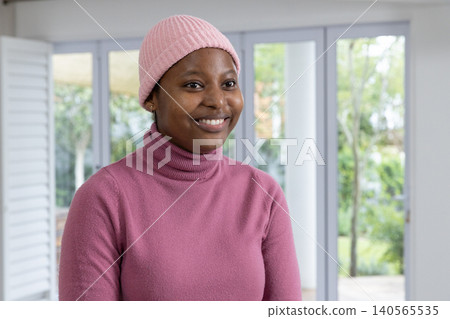 African American woman standing in bright room by glass doors wearing pink beanie and turtleneck African American woman standing in bright room by glass doors wearing pink beanie and turtleneck 140565535