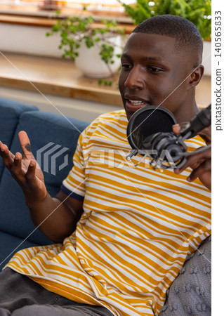 African american man speaking into podcast microphone on boom arm in home studio on sofa 140565833