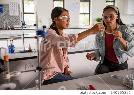 Two female students in lab wearing safety goggles and examining test tube rack Two female students in lab wearing safety goggles and examining test tube rack 140565835