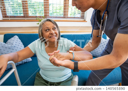 Senior african american woman gripping walker, asian caregiver supporting on sofa at home 140565890