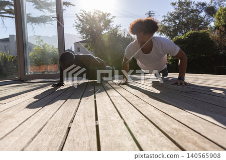 Diverse male friends doing push-ups on wooden deck patio by sliding glass door Diverse male friends doing push-ups on wooden deck patio by sliding glass door 140565908