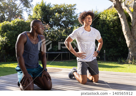 Diverse male friends kneeling on wooden deck in backyard resting after workout 140565912