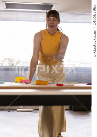 Woman in sleeveless top leaning over table in office guiding brainstorming with sticky notes 140565966