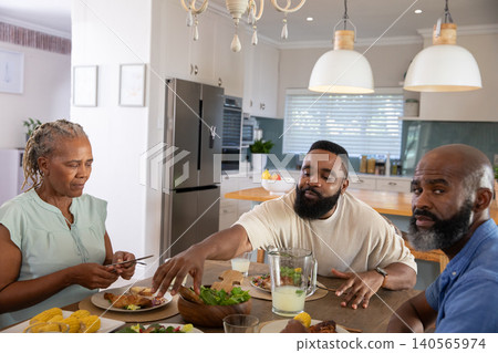 African American family reaching for salad and fried chicken on wooden dining table in kitchen African American family reaching for salad and fried chicken on wooden dining table in kitchen 140565974