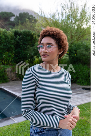African american woman standing beside pool on deck in backyard wearing shirt and glasses African american woman standing beside pool on deck in backyard wearing shirt and glasses 140566036