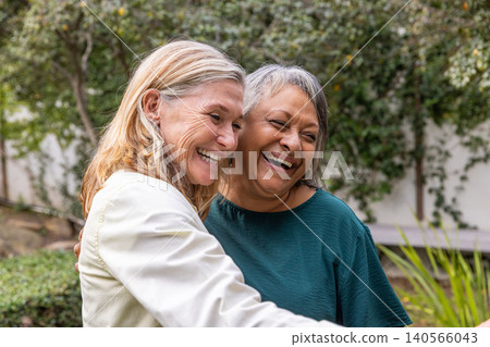 Diverse female friends hugging each other in residential garden with lush greenery backdrop Diverse female friends hugging each other in residential garden with lush greenery backdrop 140566043