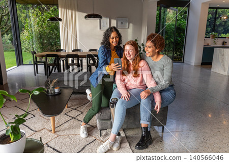 Diverse female friends sitting on bench in living area with smartphone showing prosthetic leg Diverse female friends sitting on bench in living area with smartphone showing prosthetic leg 140566046