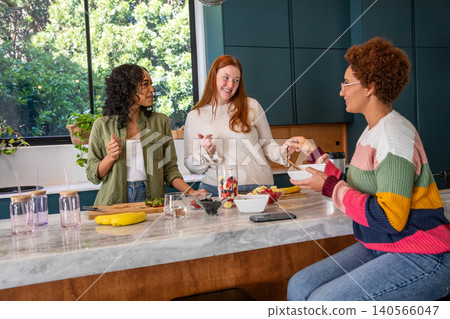 Diverse female friends chopping strawberries in kitchen using blender for smoothie 140566047