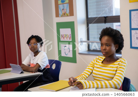 African american classmates sitting at desks tapping tablet, writing with pencil in classroom 140566063