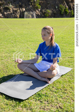 Asian girl meditating on yoga mat on grass field near white soccer goal, copy space Asian girl meditating on yoga mat on grass field near white soccer goal, copy space 140566068