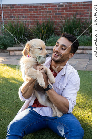 Man cross-legged on backyard lawn with golden retriever puppy with tennis ball Man cross-legged on backyard lawn with golden retriever puppy with tennis ball 140566071
