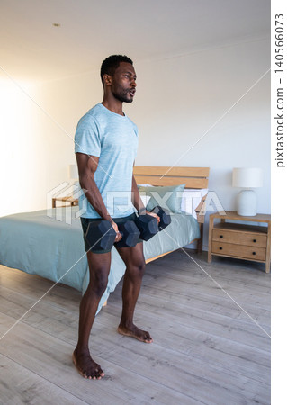 African american man with hexagonal dumbbells stretching on wooden floor in bedroom, copy space African american man with hexagonal dumbbells stretching on wooden floor in bedroom, copy space 140566073