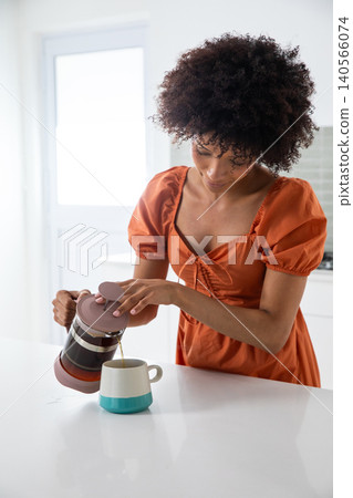 African american woman pouring coffee from french press into mug at kitchen counter African american woman pouring coffee from french press into mug at kitchen counter 140566074