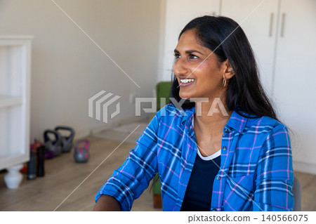 Asian indian woman sitting in home gym smiling near kettlebells, copy space Asian indian woman sitting in home gym smiling near kettlebells, copy space 140566075