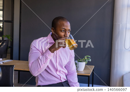African american man sitting on table sipping beer from mug in office lounge, copy space African american man sitting on table sipping beer from mug in office lounge, copy space 140566097