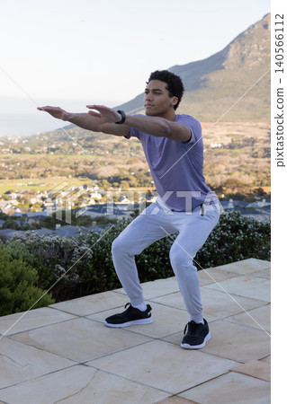 African american man squatting on stone patio with valley view fitness tracker and sneakers African american man squatting on stone patio with valley view fitness tracker and sneakers 140566112