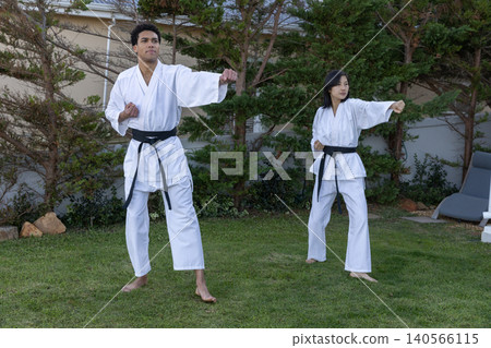 Diverse karate partners standing in backyard wearing white gi with belts practicing punches Diverse karate partners standing in backyard wearing white gi with belts practicing punches 140566115
