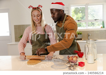 Diverse couple wearing olive aprons rolling cookie dough with wooden rolling pin in modern kitchen Diverse couple wearing olive aprons rolling cookie dough with wooden rolling pin in modern kitchen 140566214