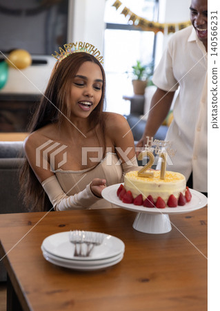 African american friends celebrating birthday leaning over table at home with cake, balloons African american friends celebrating birthday leaning over table at home with cake, balloons 140566231