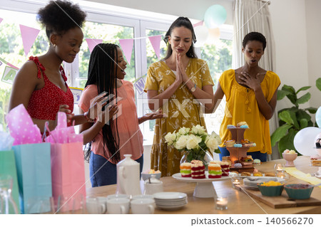 European American woman wearing mustard dress making wish at dining table with cakes and cupcakes European American woman wearing mustard dress making wish at dining table with cakes and cupcakes 140566270