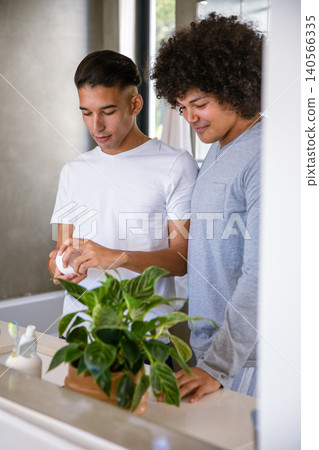 Diverse male friends opening grooming jar at bathroom counter next to toothbrush holder and plant Diverse male friends opening grooming jar at bathroom counter next to toothbrush holder and plant 140566335