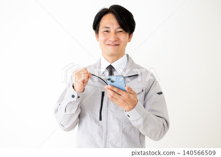 A middle-aged businessman in gray work clothes makes a triumphant gesture while holding his smartphone against a white background. A middle-aged businessman in gray work clothes makes a triumphant gesture while holding his smartphone against a white background. 140566509